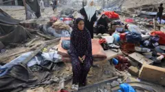 A Palestinian woman sits amidst debris as people inspect the site of an Israeli strike on a house in Gaza City, 30 July 2026.
