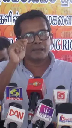 කණ්නාඩි දැමූ පුද්ගලයෙකු මාධ්‍ය හමුවක කතා කරනු පෙනේ.