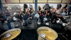 نازحون فلسطينيون في غزة يتجمعون في محاولة للحصول على طعام، تظهر في الصورة التي التقطت نهاراً أوعية طعام وحشود