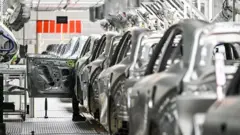 Funcionário inspeciona um carro elétrico em uma fábrica da Zeekr na Ilha Meishan, em Ningbo, na província de Zhejiang, no leste da China, em 18 de abril de 2025. A foto mostra uma fileira de veículos prateados em uma fábrica