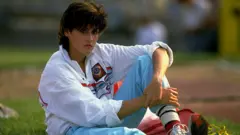 A atleta soviética Galina Chistyakova descansa sentada sobre a grama, no intervalo de uma competição