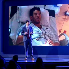 David Fajgenbaum em uma palestra. Ao fundo, imagem de um homem no hospital.