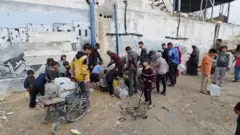 رجال ونساء وأطفال في طابور لتعبئة أوعيتهم وغالوناتهم بمياه الشرب.