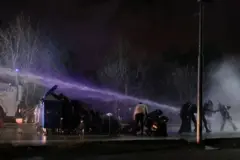 Bir grup öğrenci bir çöp kutusunun arkasında tazyikli sudan korunmaya çalışıyor