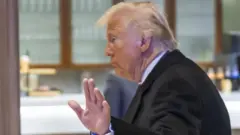 Donald Tramp u crnom odelu slikan iz profila kako odmahuje rukom