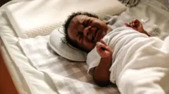 Um bebê chora no berço enquanto fecha os punhos