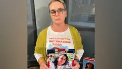 صورة لماندي داماري ترفع صورة ابنتها إيميلي داماري، المحتجزة كرهينة في قطاع غزة، خلال زيارتها إلى المملكة المتحدة.