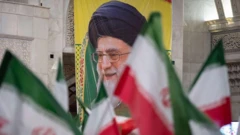 Старый человек в иранском религиозном головном уборе среди иранских флагов