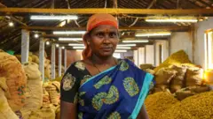 အပြာရောင်မှာ အစိမ်းရောင်ဖောက်ထားတဲ့ ဆာရီဝတ်အမျိုးသမီးတစ်ဦး မတ်တပ်ရပ်နေပြီး သူ့နောက်မှာတော့ နနွင်းပုံကြီး ရှိနေပါတယ်။ 