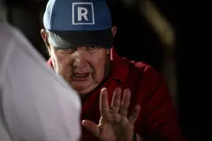 Rafael López Aliaga, con una gorra azul con el logo de su partido y la palma de la mano izquierda levantada a la altura de su pecho.