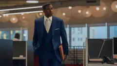 Cena do filme 'Luta de Classes', com Denzel Washington de terno e gravata, segurando pastas de trabalho