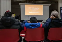 Uma criança toca no pai enquanto eles assistem a uma apresentação do Centro Amica para os Direitos dos Imigrantes (anteriormente conhecido como Coalizão CAIR) sobre política migratória em uma escola de Washington, DC, em 10 de janeiro de 2025 (Foto de ANDREW CABALLERO-REYNOLDS/AFP via Getty Images)