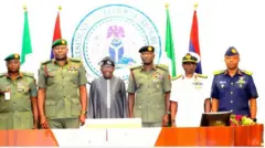 Àwọn ọ̀gá illese ológun dúró ní apá àti apa òsì ààrẹ Bola Ahmed Tinubu.