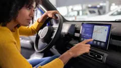Una mujer señalando una pantalla en el interior de su coche.