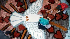 Uma mulher finalizando um dos tapetes de imagens produzidas para a celebração do Corpus Christi no Brasil.