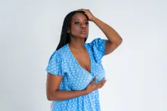 Modèle féminin grande taille posant en robe bleue sur fond gris, jeune grosse femme africaine avec une silhouette sinueuse et une coiffure en queue de cochon