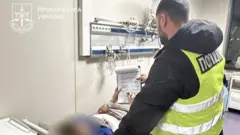 Поліцейський надає документ на підпис підозрюваному, який лежить на ліжку