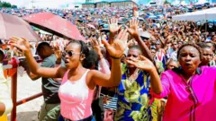 Imbaga y'abantu barimo gusenga baririmba, barimo n'abitwikiriye imitaka, inyuma yabo kure hari ingoro