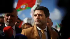 André Ventura olhando para o lado. Há várias pessoas em volta e uma bandeira de Portugal ao fundo