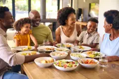 Famille multigénérationnelle assise autour d’une table mangeant un repas à la maison ensemble