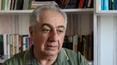 Gubad Ibadoglu sits in green t shirt in front of bookcase