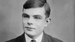 Uma fotografia em preto e branco de Alan Turing, um jovem com cabelo escuro penteado para um lado. Ele olha para algo ligeiramente fora do enquadramento com uma expressão neutra.