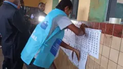 Umukozi w'akanama k'amatora arimo kumanika intonde z'abatora ku biro by'amatora i Kinshasa