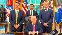 Flavio Bolsonaro, Paulo Figueiredo e Eduardo Bolsonaro de pé, em volta de Trump, que está sentado, em sua mesa no Salão Oval