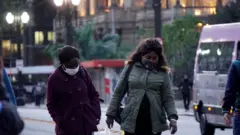 Duas mulheres caminham usando máscara contra covid-19 e roupas de frio no centro de São Paulo, no fim de tarde