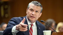 Pete Hegseth gesticula durante uma audiência no Senado. Ele veste terno azul-marinho e gravata listrada em vermelho e cinza