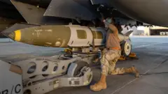A US airman in brown mattaches a munitions system to an F-15 fighter jet taking part in Operation Hawkeye Strike. Photo: 19 December 2025
