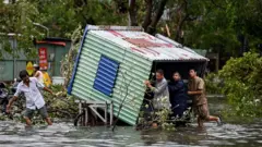 စူပါတိုင်ဖွန်းမုန်တိုင်း ယာဂီ တိုက်ခတ်အပြီး အပျက်အစီးတွေကို ဒူးခေါင်းနီးနီး ရောက်နေတဲ့ ရေတောထဲမှာ သယ်ယူနေကြတဲ့ အမျိုးသား ၄ ဦးကို တွေ့ရတာဖြစ်ပါတယ်။ သူတို့အနောက်မှာတော့ မုန်တိုင်းကြောင့် ပြိုလဲသွားတဲ့သစ်ပင်အချို့ကို မြင်တွေ့ရပါတယ်။ 