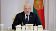 Александр лукашенко за столом на фоне флага
