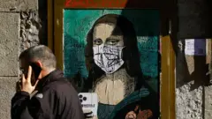 A man in Barcelona (Catalonia) walks past a poster depicting Leonardo da Vinci's Mona Lisa wearing a facemask, by Italian urban artist Salvatore Benintende
