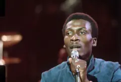Jimmy Cliff durante show em 1974. Ele está segurando um microfone e cantando