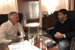 يجلس جبر بن يوسف آل ثاني على اليمين مرتديا قميصا أزرق اللون، بينما يجلس جيفري إبستين على اليسار ويرتدي قميصا أبيض اللون، وتتوسطها طاولة عليها زجاجات وهواتف محمولة وأوراق 