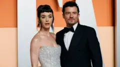 Katy Perry with Orlando Bloom for di Vanity Fair Oscars party. She dey wear a shoulderless silver dress, while di man dey wear a traditional black and white tuxedo. 