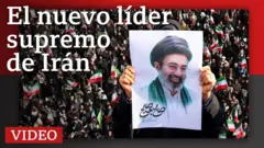 Una persona sostiene un retrato de Mojtaba Jamenei en primer plano, de fondo una multitud agita banderas de Irán
