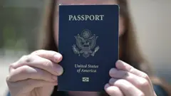 A woman hold her US passport, blocking her face with it.