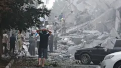 Pessoas observam os danos a prédios na Praça Nobonyad após os ataques aéreos israelenses em 13 de junho de 2025 em Teerã, Irã