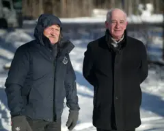 Rein Klaar (à esquerda) e Jaan Krinal (à direita) fotografados na Estônia. Eles vestem casacos de inverno escuros em meio à neve. Rein está com o capuz levantado e usa luvas grossas.