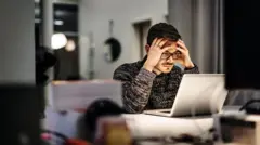 Homem olhando para a tela do computador. Ele está com as mãos na cabeça