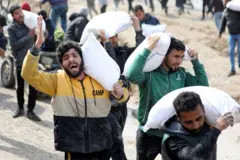 فلسطينيون يحملون أكياس دقيق انتزعوها من شاحنة مساعدات بالقرب من نقطة تفتيش إسرائيلية،  في مدينة غزة، 19 فبراير/ شباط 2024
