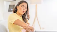 Mulher examina o cotovelo com dores