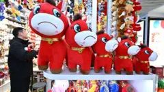 Loja de brinquedos mostra uma fileira de cavalos de brinquedo vermelhos. Um deles está com um sorriso costurado de cabeça para baixo.