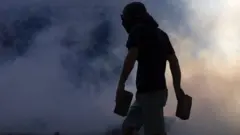 Vulto de homem mascarado em meio a fumaça na rua