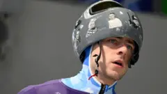 Vladislav Geraskevič nosi kacigu sa slikama poginulih u ratu u Ukrajini na stazi za skeleton u Kortini, u Italiji, na Zimskim olimpijskim igrama