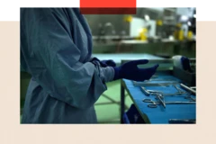 Un cirujano se pone un par de guantes mientras está de pie frente a una mesa sobre la que se han colocado instrumentos quirúrgicos.