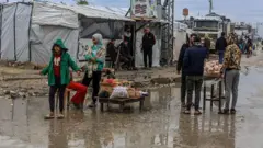 فلسطينيون يقفون وسط برك من مياه الأمطار أمام خيام لا تحميهم من الأمطار الغزيرة والرياح العاتية التي تجتاح قطاع غزة