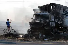 Um homem de bicicleta tira uma foto ao lado de um caminhão incendiado em Jalisco.